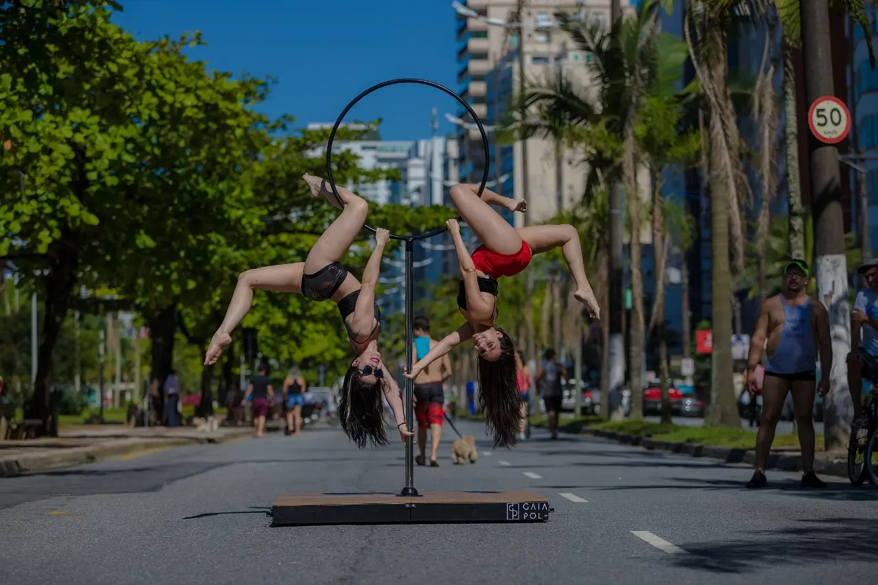 Duas profissionais praticando pole dance em um palco desmontável no meio da rua.